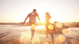 Glückliches Paar läuft durch flaches Wasser am Strand.
